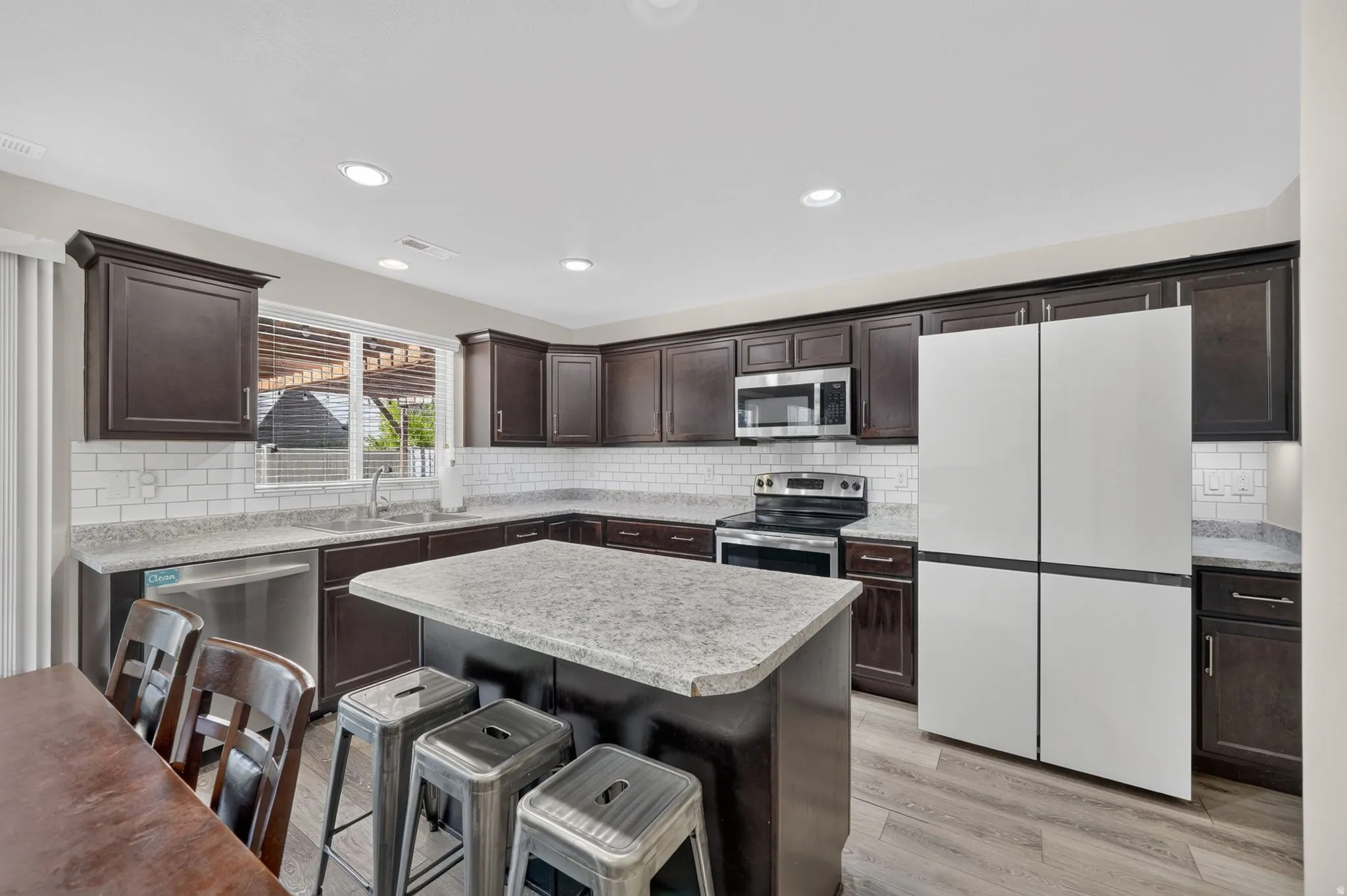 Kitchen with wood-finish flooring, dark wood cabinetry, light-toned countertops, subway tile backsplash, and recessed lighting