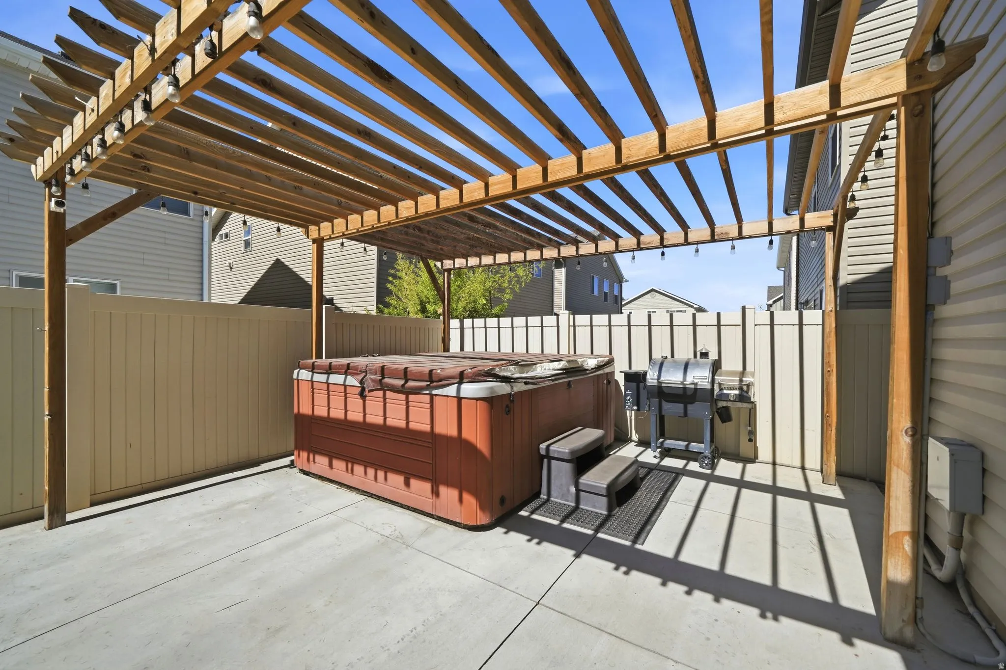 Paved patio featuring a wood pergola with string lighting and a built-in hot tub