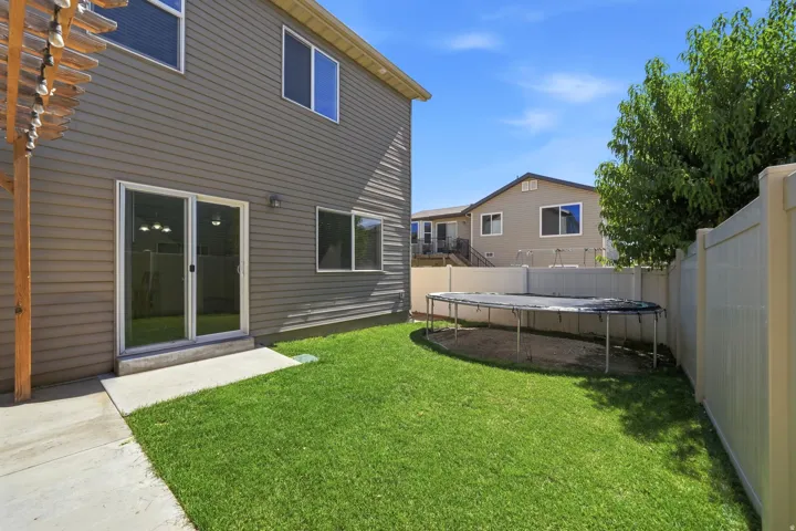 Expansive grassy backyard featuring a concrete patio, sliding glass door access, and privacy fencing