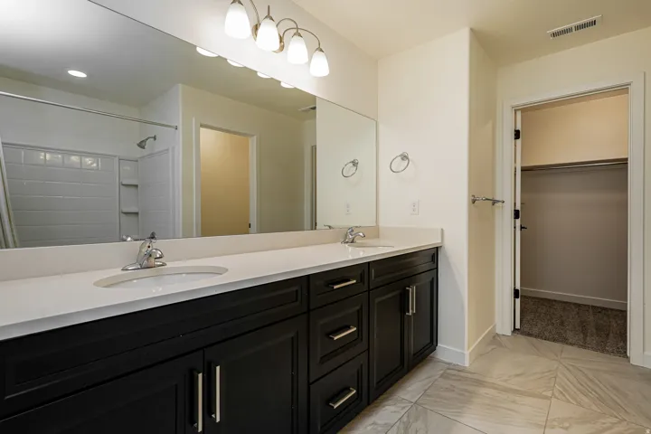 Dual vanity with dark wood-finish cabinetry, chrome fixtures, and a spacious mirror