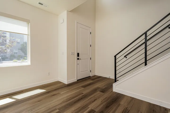 LVP flooring, white paneled door, modern black metal staircase railing, neutral wall finishes, and a roller shade window treatment