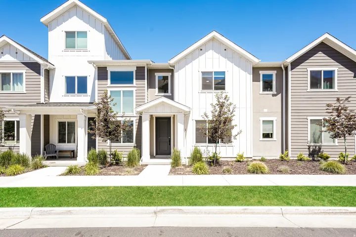 Modern townhome with board and batten siding, multiple windows, covered entryways, and manicured landscaping