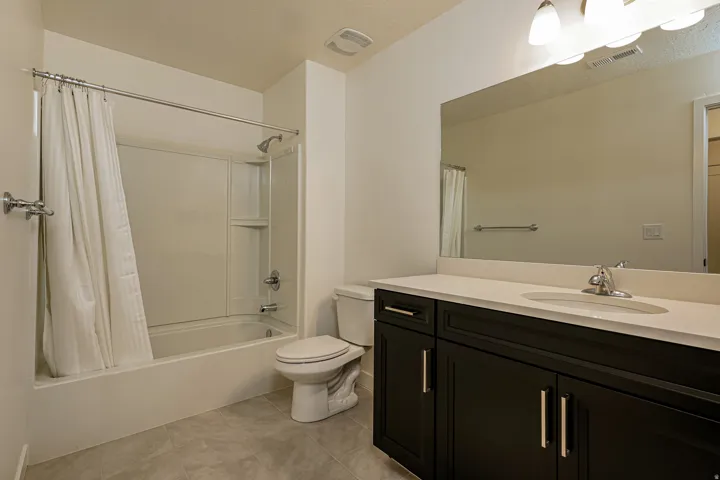 White bathtub and shower combination with a single-handle faucet, dark wood-finish vanity with a light-toned countertop, and tile flooring