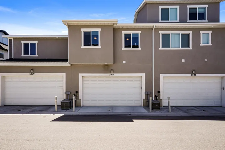 Multi-level stucco exterior with multiple single-car garages, white window frames, and exterior lighting fixtures