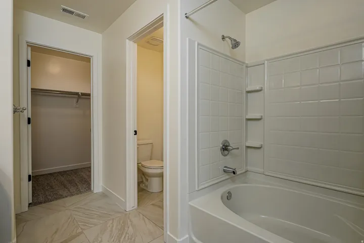 Bathtub with subway tile surround and integrated shelving, chrome fixtures, separate water closet, and tile flooring