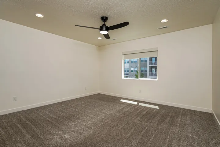 Spacious room featuring textured carpet flooring, a window with roller shades, a ceiling fan with integrated lighting, and recessed ceiling lights