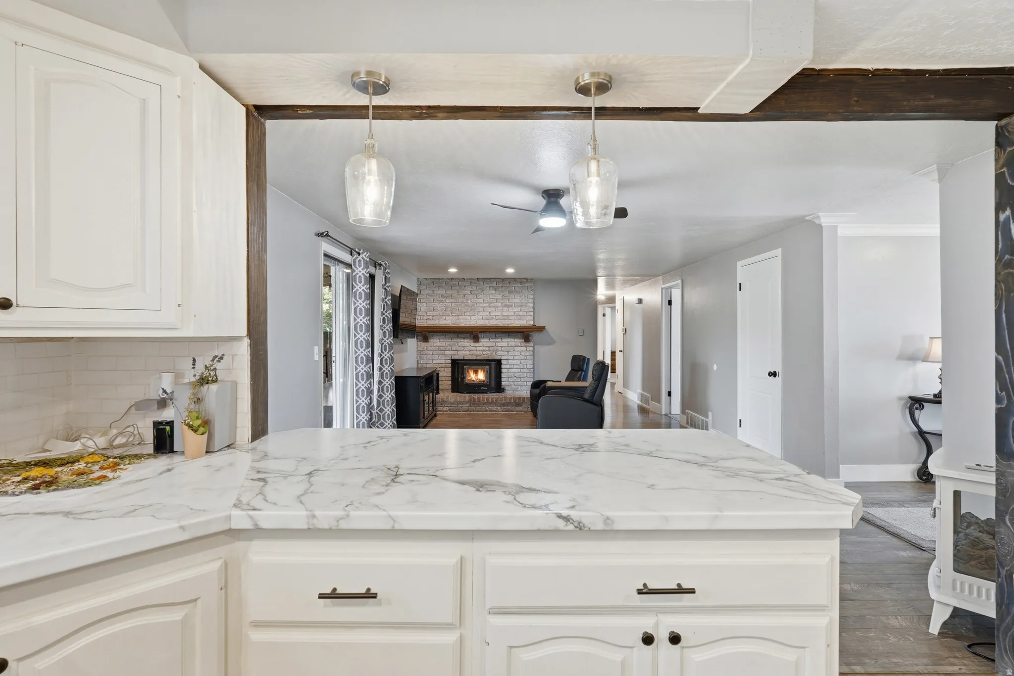 Kitchen island with a marbled countertop, white cabinetry, and pendant lighting