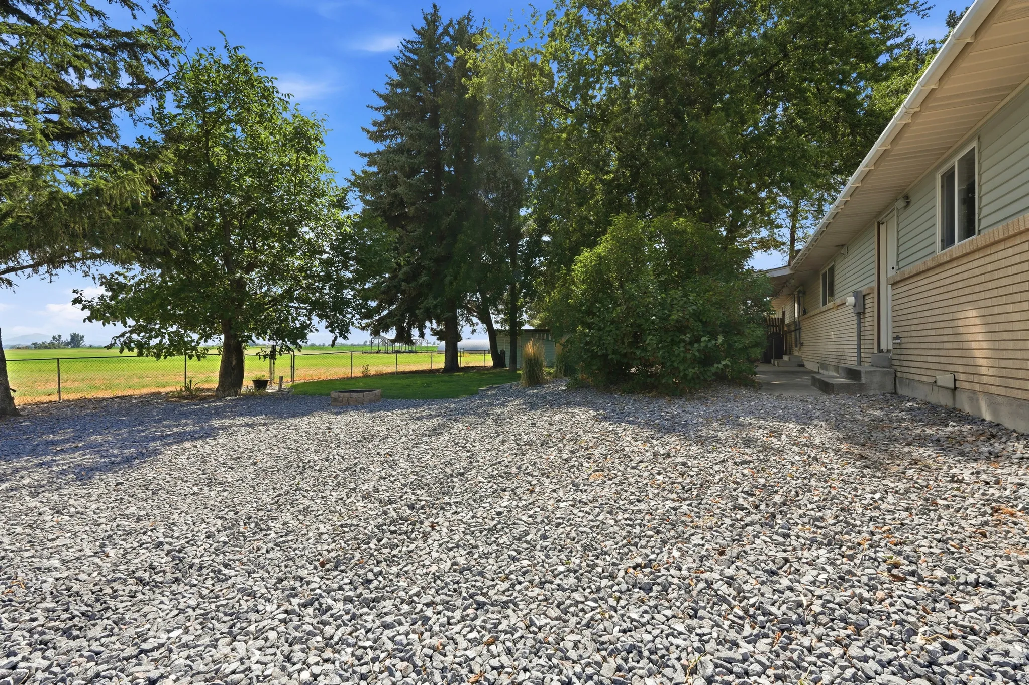 Expansive gravel area with mature trees, green lawn, and a light-colored brick and siding exterior