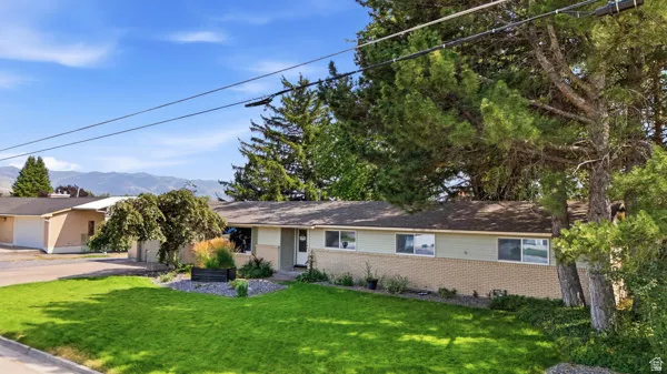 Ranch-style exterior with brick and siding, featuring a neatly maintained lawn, mature front yard trees, and mountain scenery