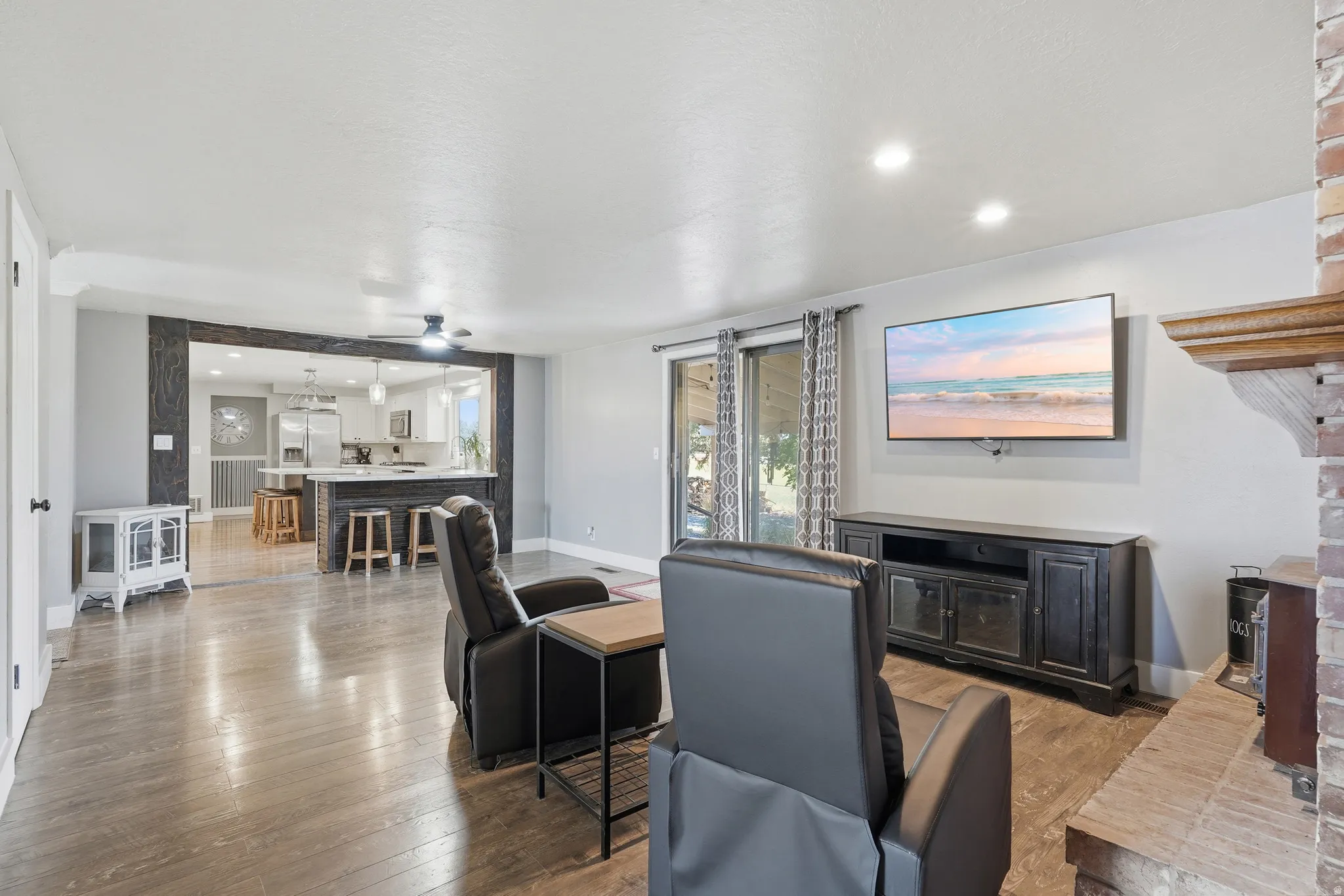 Open-concept living area featuring wood-finish flooring, recessed lighting, and a prominent brick fireplace