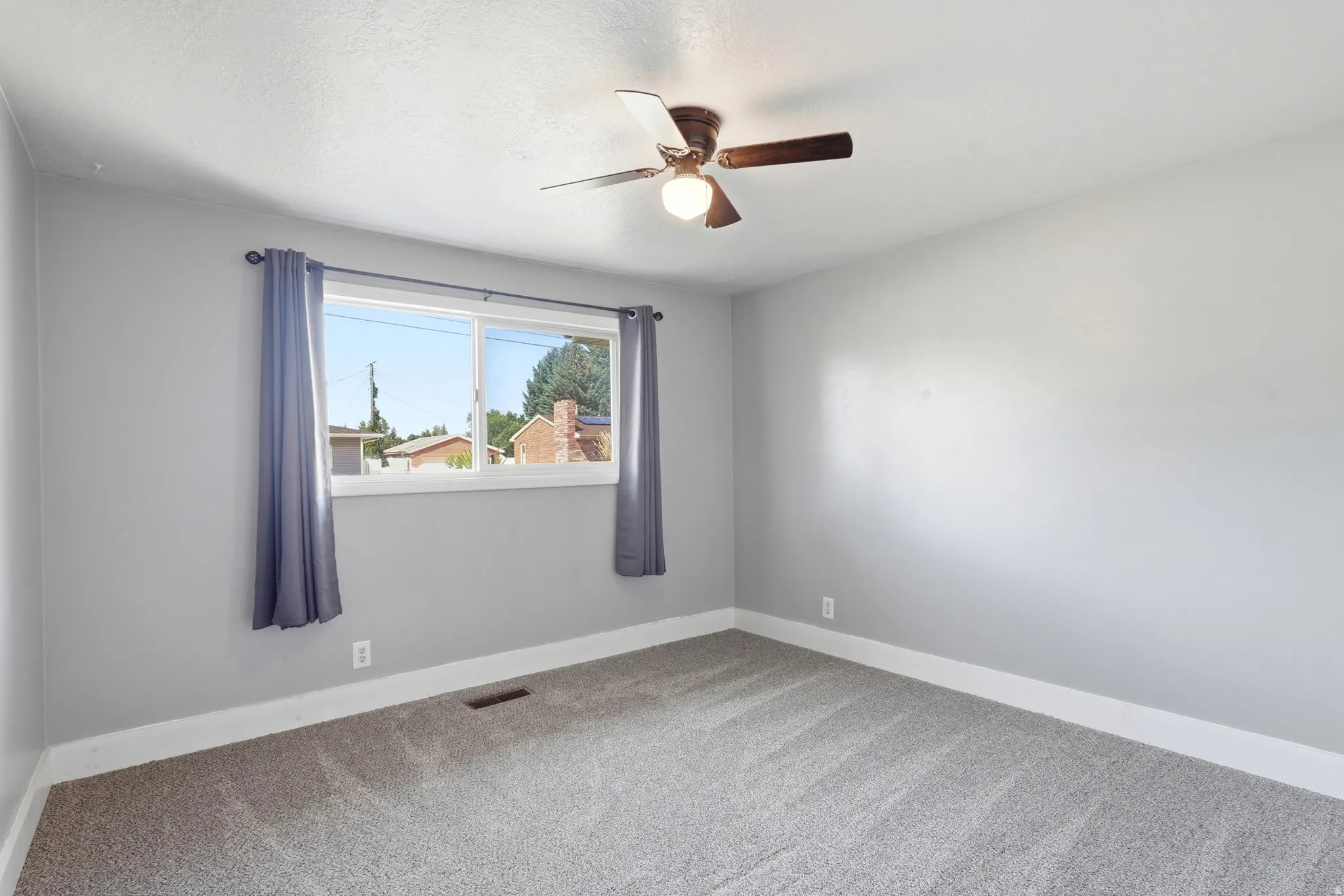 Neutral gray wall paint, light gray carpeting, white trim, a large window, and a ceiling fan with integrated lighting