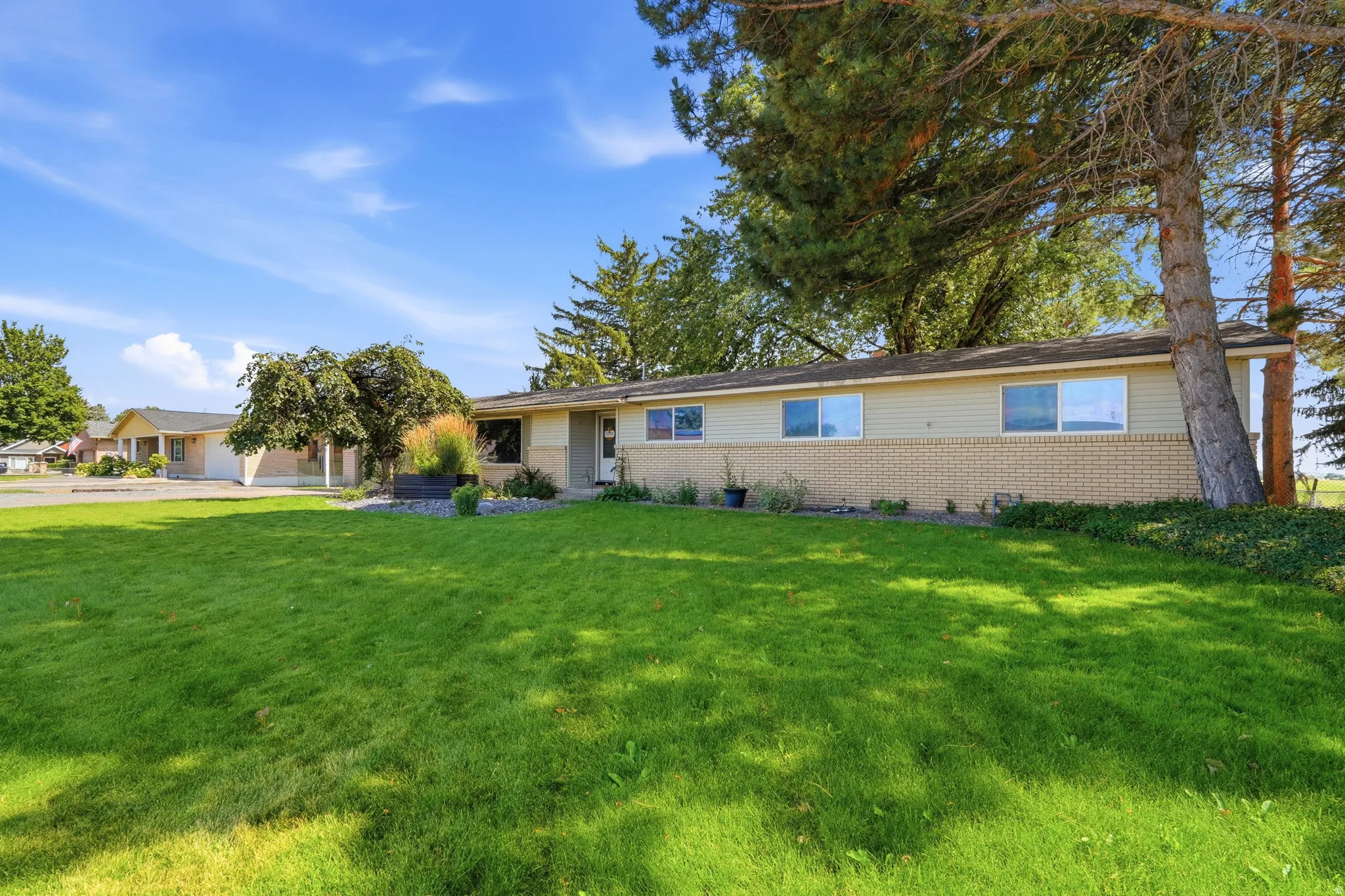 Ranch-style exterior with a brick and siding facade, mature trees, and an expansive lawn