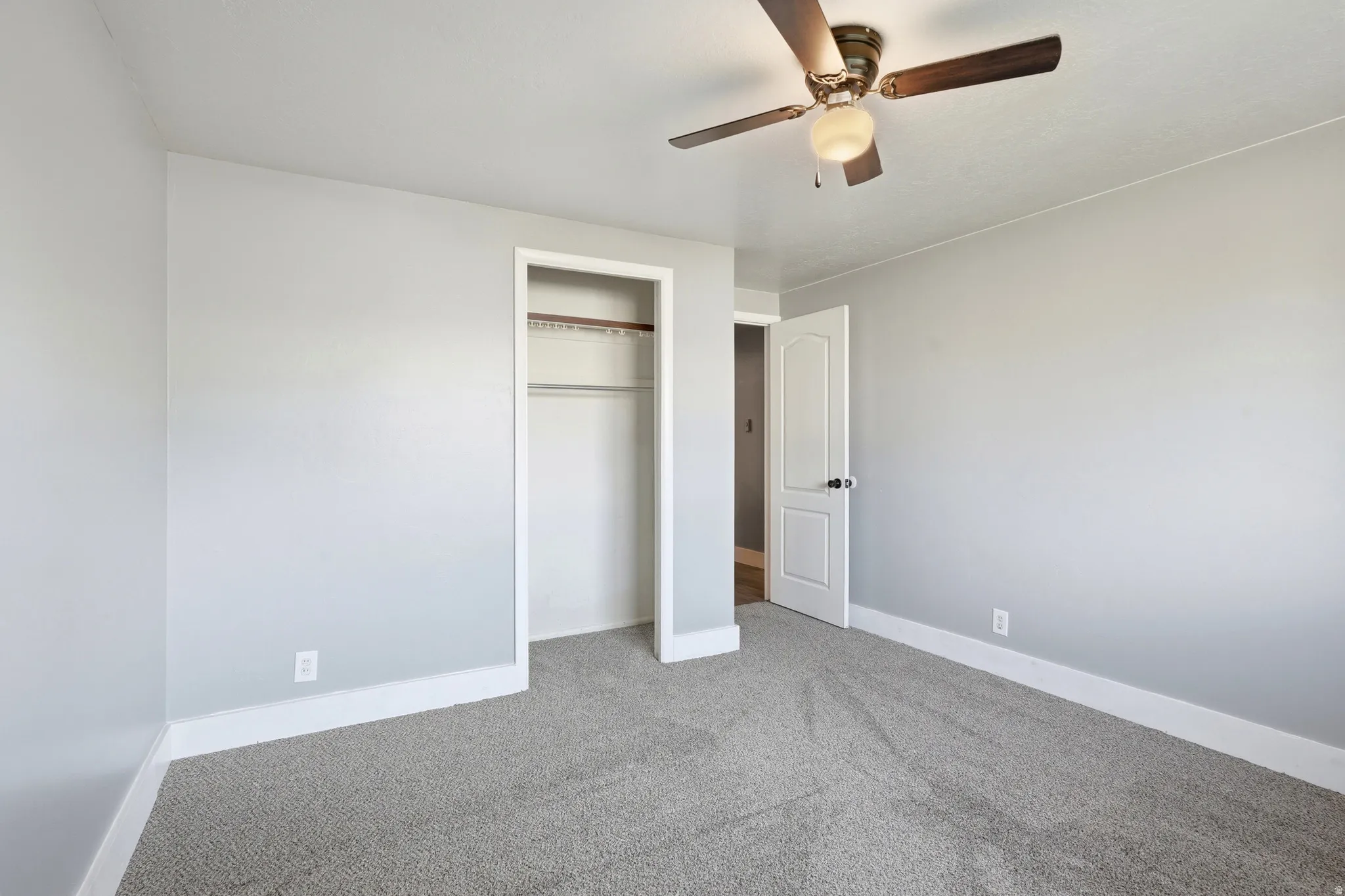 Carpeted flooring, light gray wall tones, ceiling fan, white trim, and a built-in closet with shelving