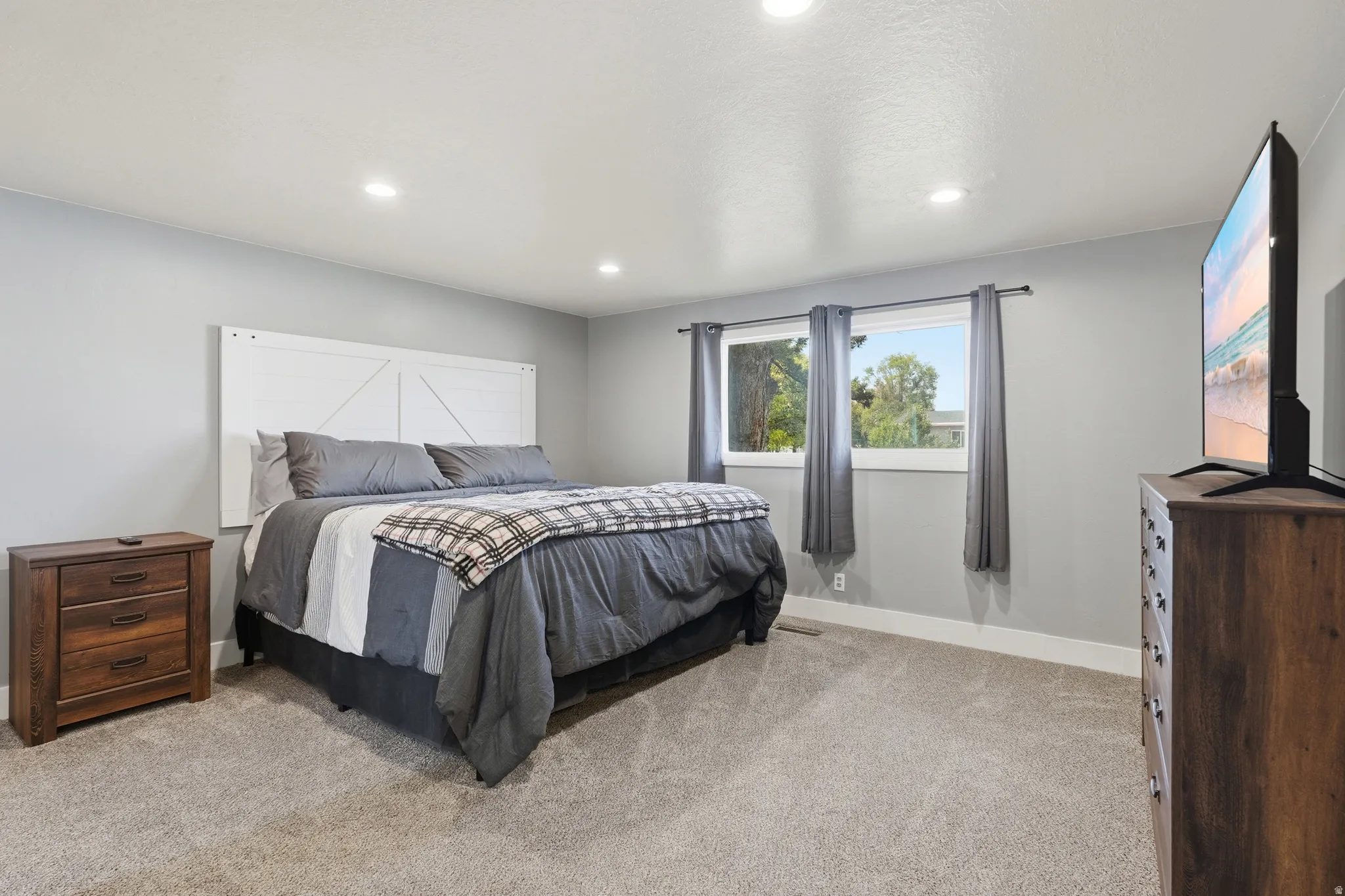 Recessed lighting illuminates the space, featuring light gray walls, plush carpeting, and dual windows