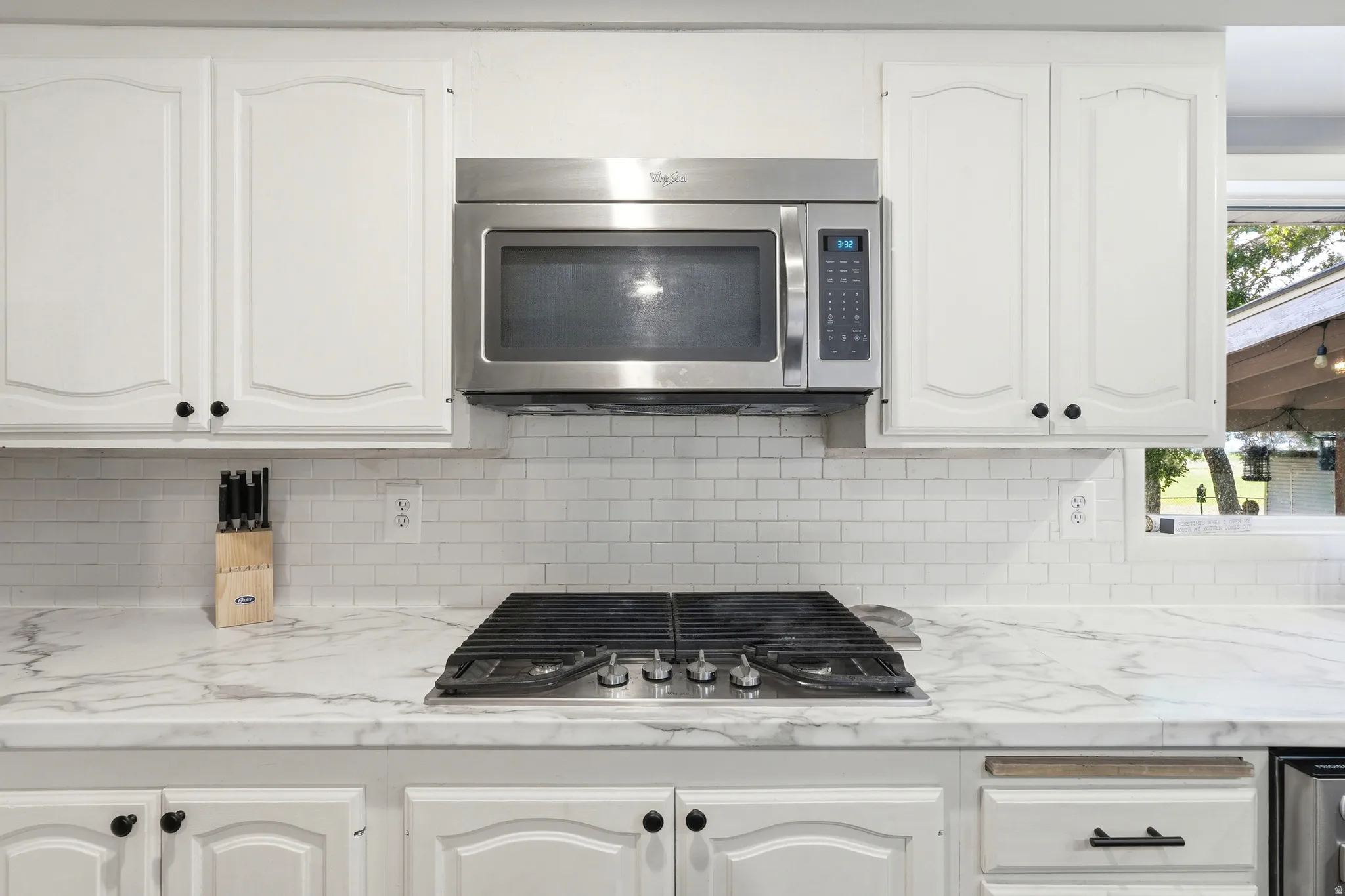 Built-in stainless steel microwave, white cabinetry with black hardware, integrated gas cooktop, white subway tile backsplash, and stone-finish countertops