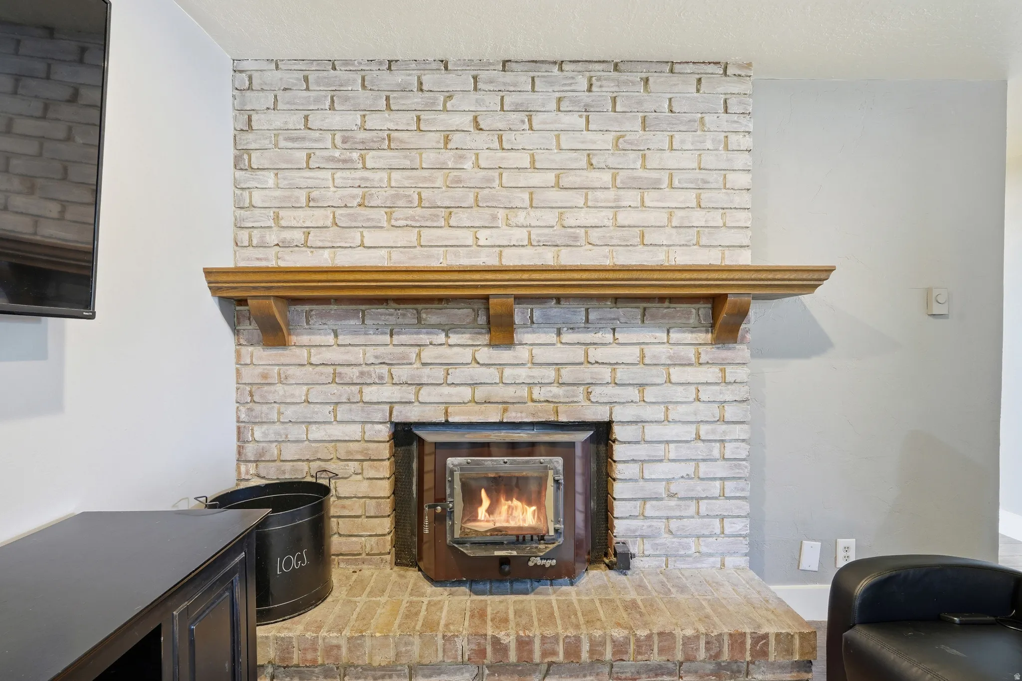 Whitewashed brick fireplace with a wood-burning insert and a substantial wood mantel