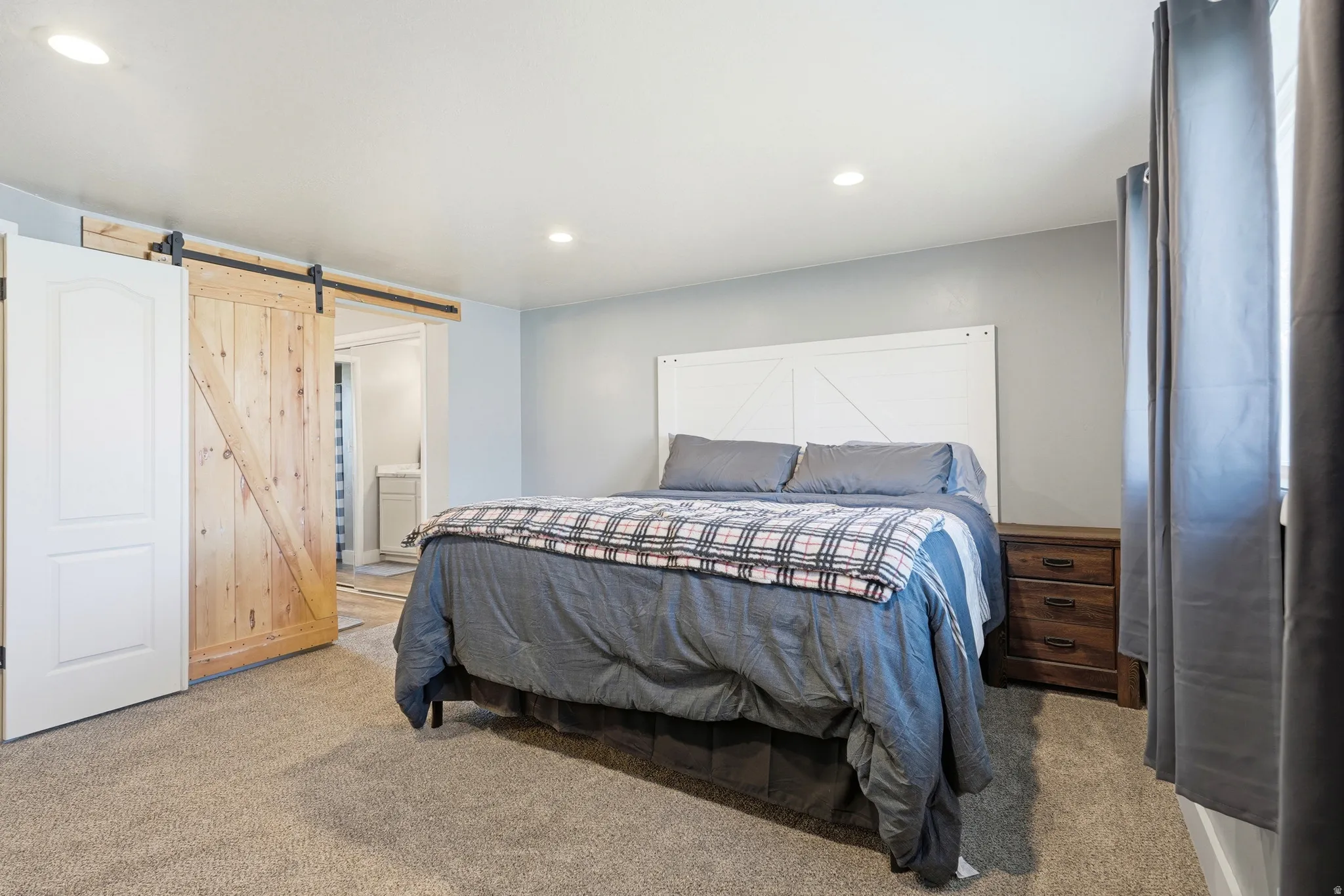Carpeted flooring, recessed lighting, and a barn door entry to an adjoining area