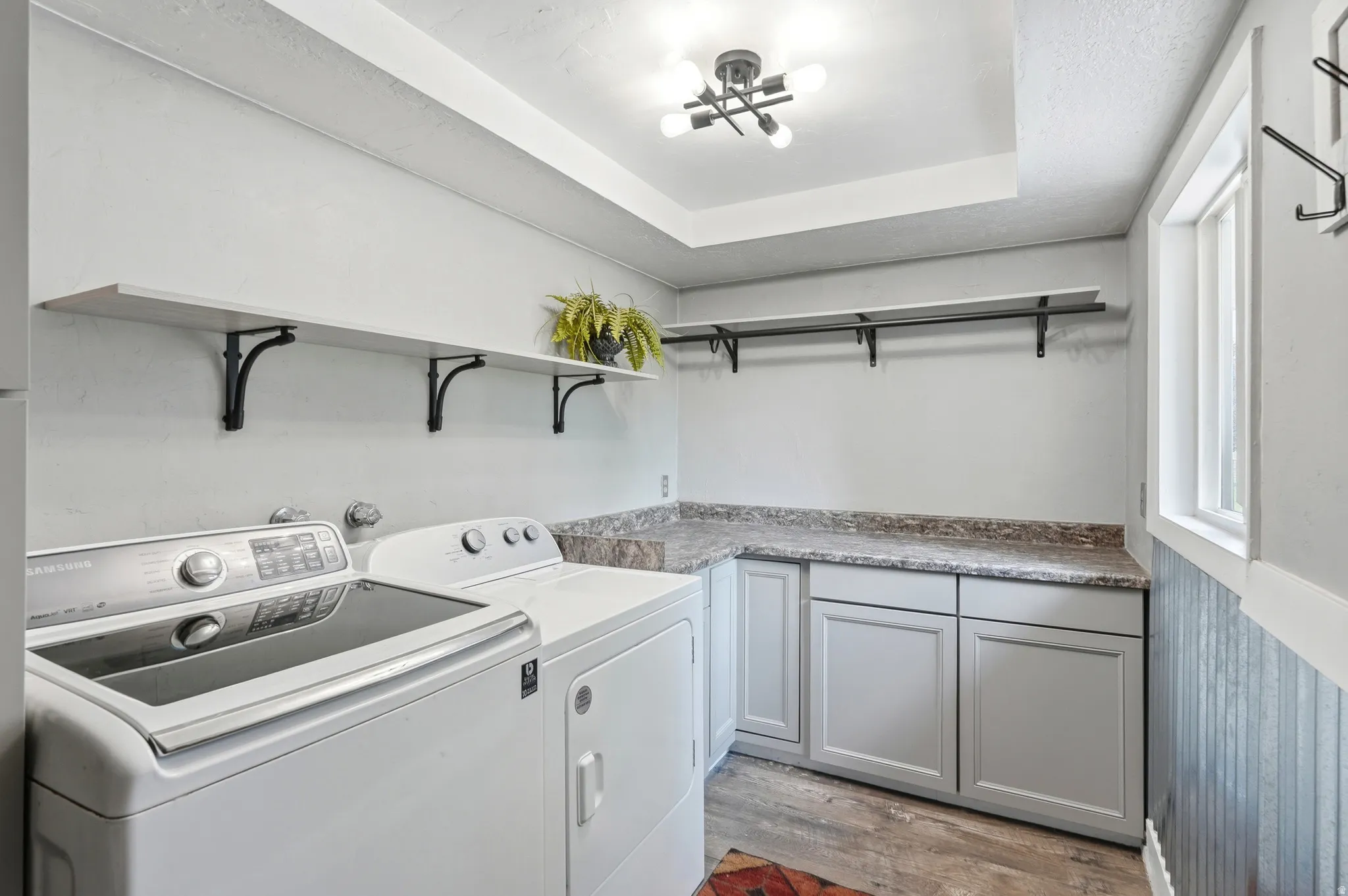 Laundry area featuring wood-finish flooring, built-in cabinetry with a countertop, open shelving, and a window