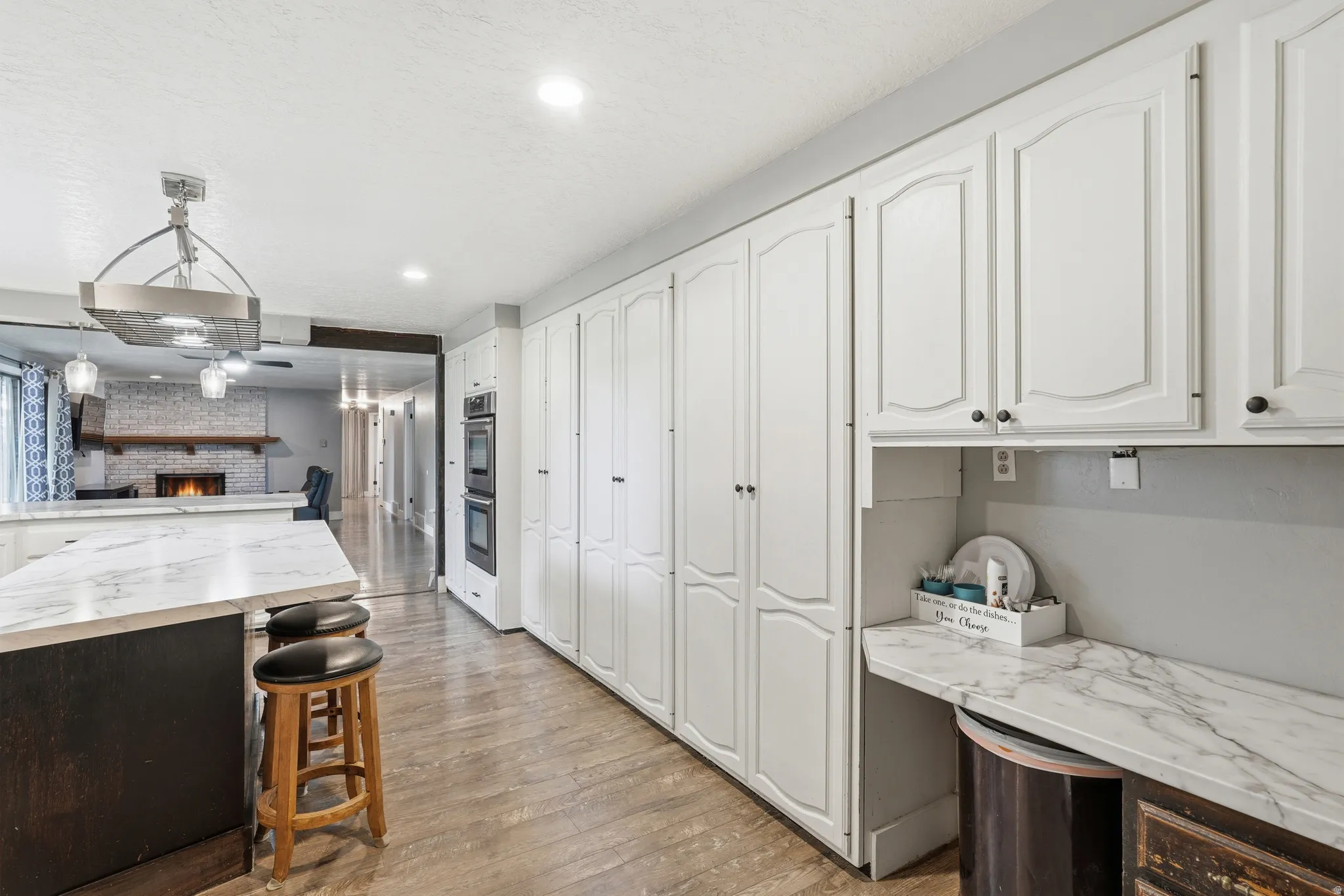 Expansive kitchen with wood-finish flooring, white cabinetry, integrated double ovens, and a marble-finish island countertop