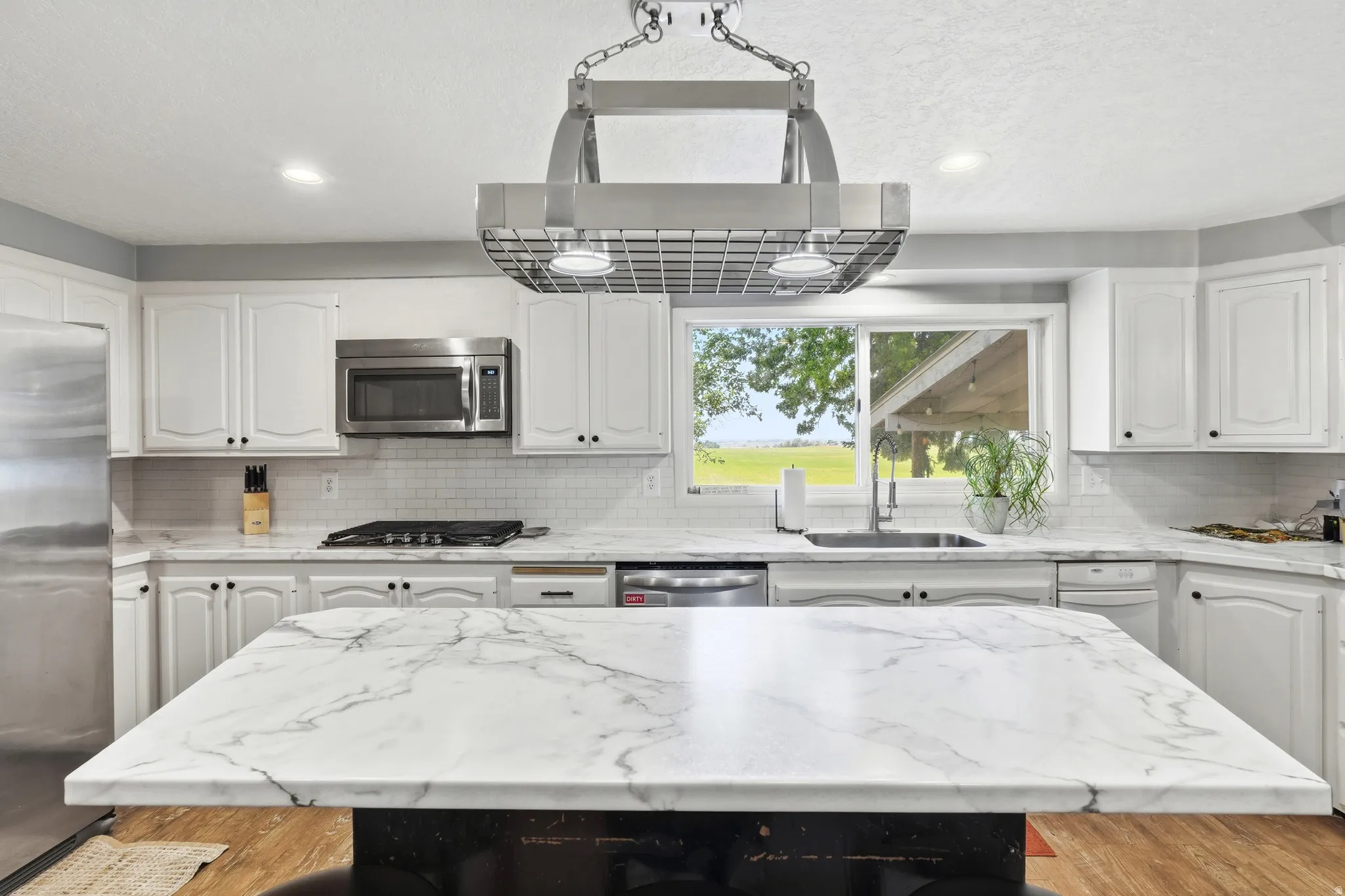 White cabinetry, stainless steel appliances, large kitchen island with a marbled surface, subway tile backsplash, and recessed lighting