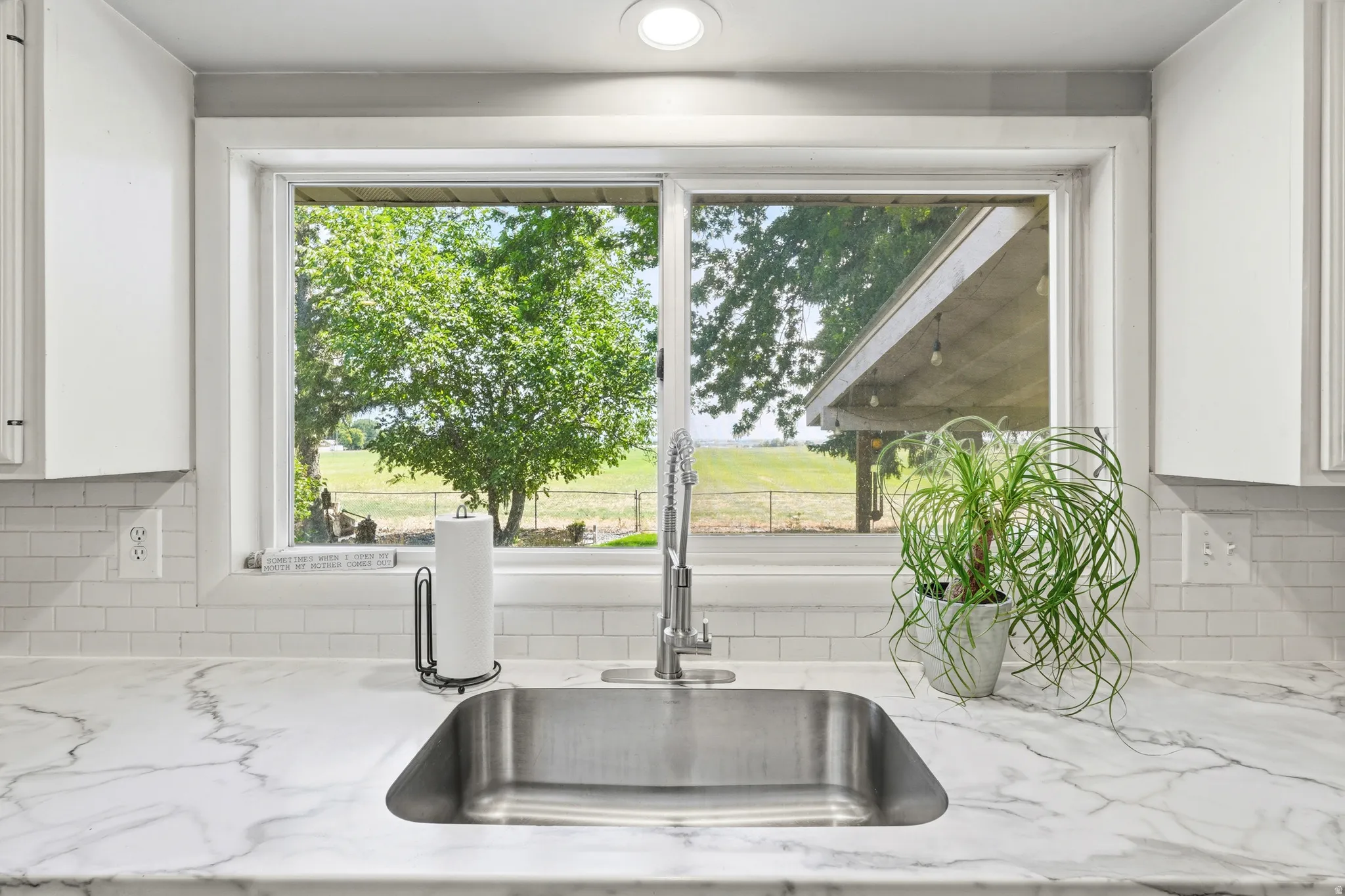 Undermount stainless steel sink, pull-down faucet, white marble-look countertop, white subway tile backsplash, and white cabinetry