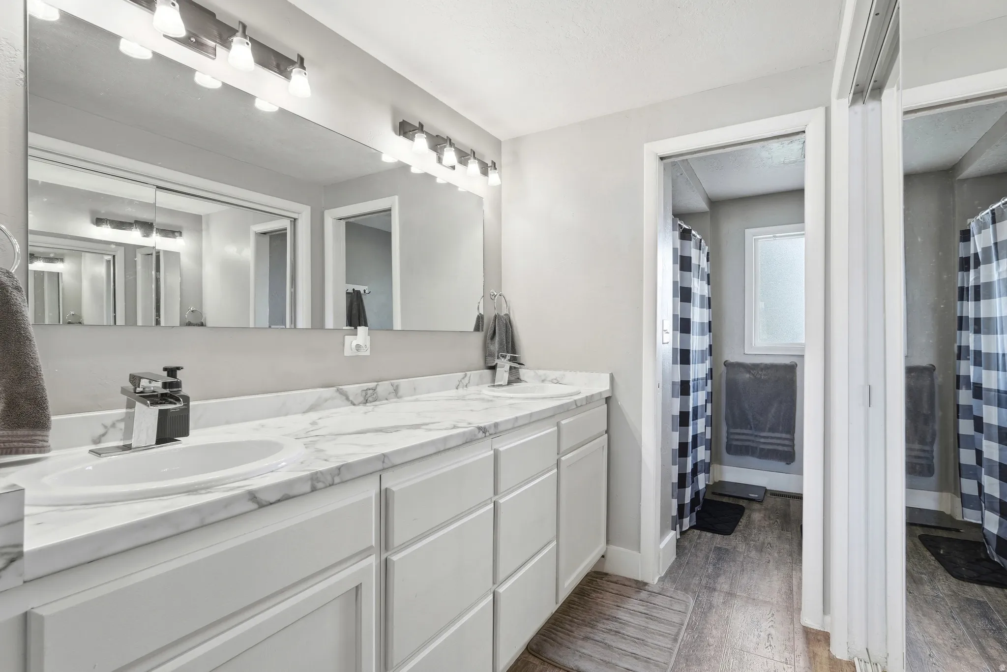 Dual sink vanity with stone-finish countertop, white cabinetry, and a full-width mirror