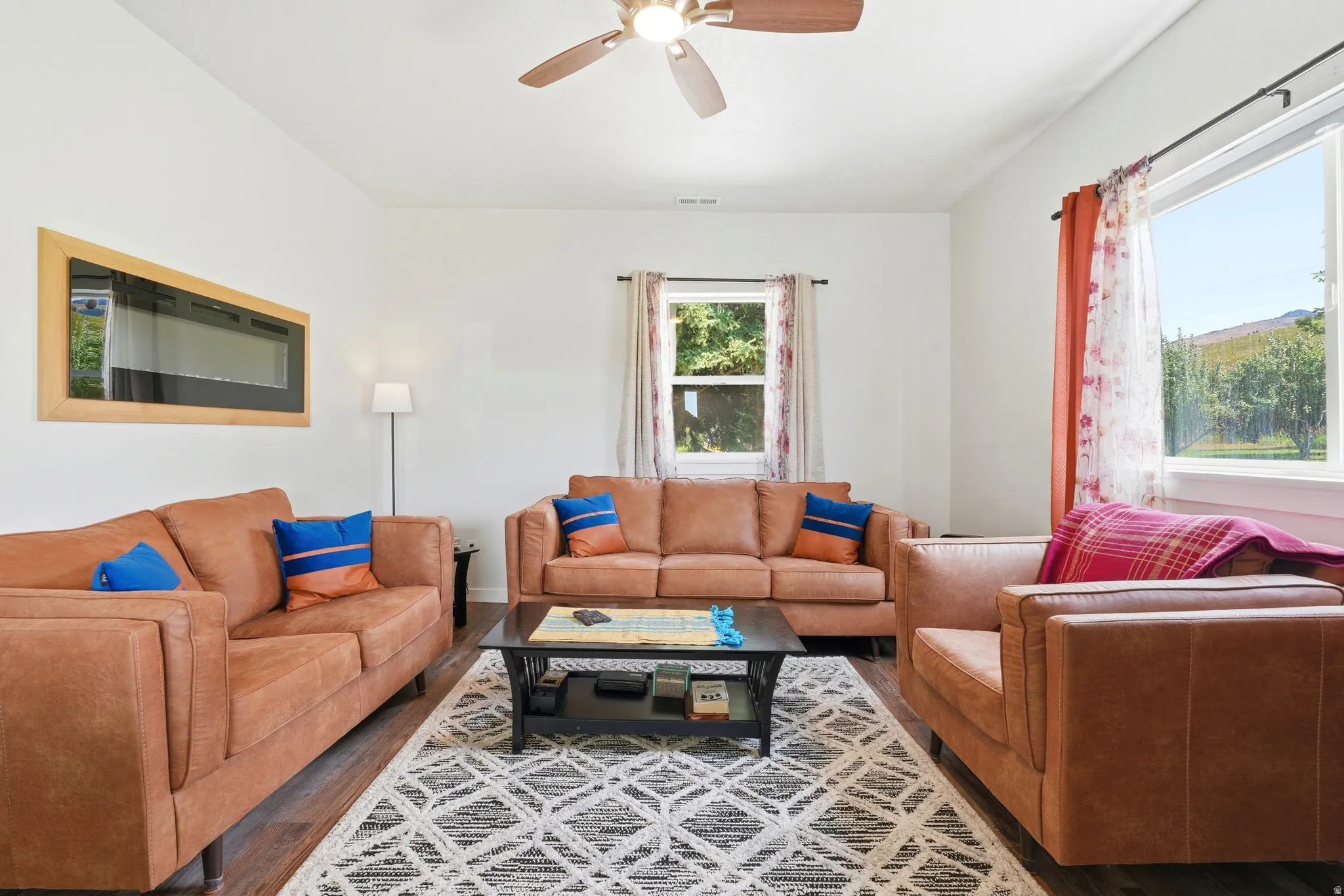 Spacious living area featuring wood-finish flooring, a ceiling fan, and large windows