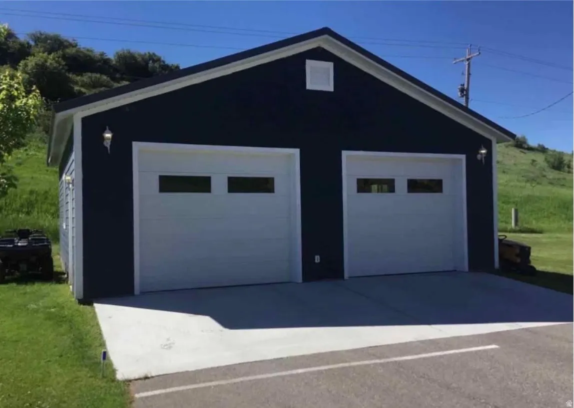 Detached structure featuring dark-colored siding, two garage doors with window panels, and concrete driveway