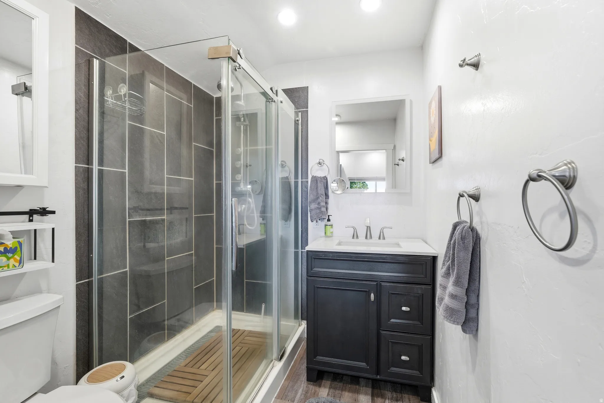 Glass-enclosed shower with dark tile surround, dark wood-finish vanity with countertop, and undermount sink