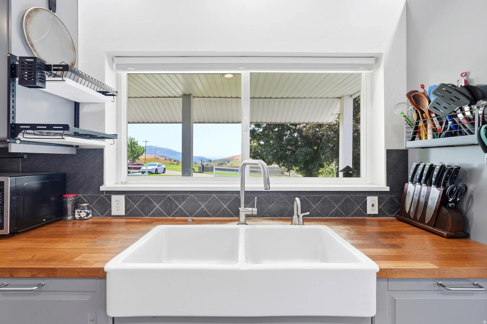 Wood-finish countertops, ceramic farmhouse sink with a gooseneck faucet, and diamond-patterned tile backsplash
