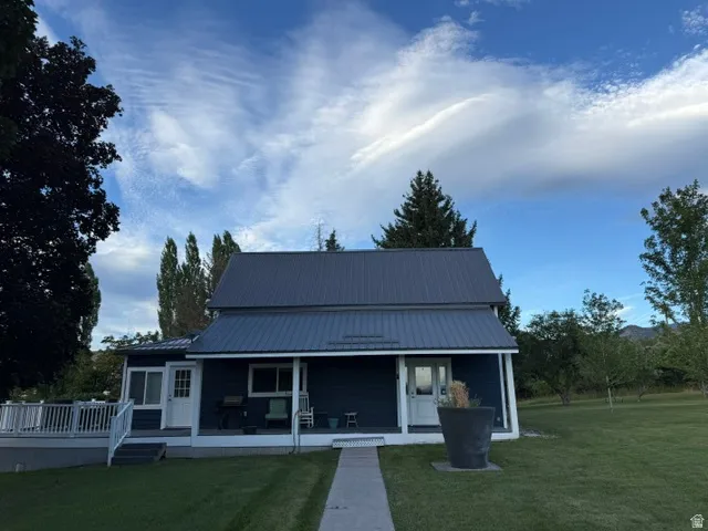 Blue siding exterior with a dark metal roof, featuring a covered front porch, a side deck with white railings, and a concrete walkway