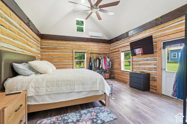 Vaulted white ceiling with a ceiling fan, wood-finish flooring, exposed log walls, window with outdoor scenery, and an exterior door with glass paneling
