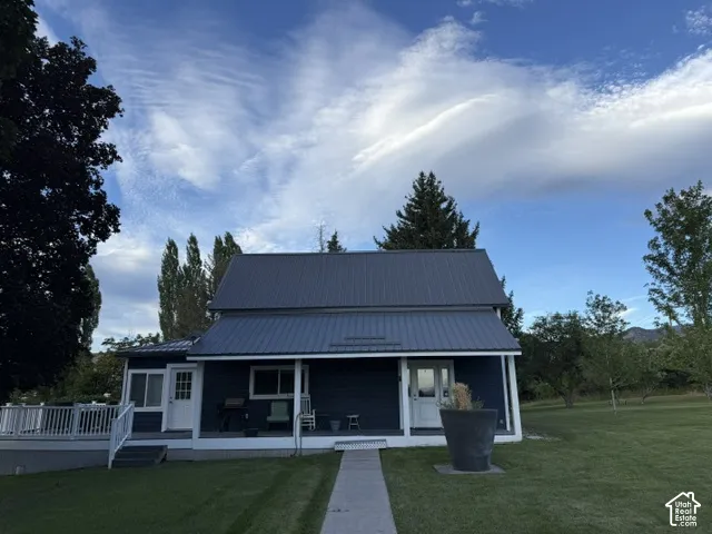 Blue siding exterior with a dark metal roof, featuring a covered front porch, a side deck with white railings, and a concrete walkway