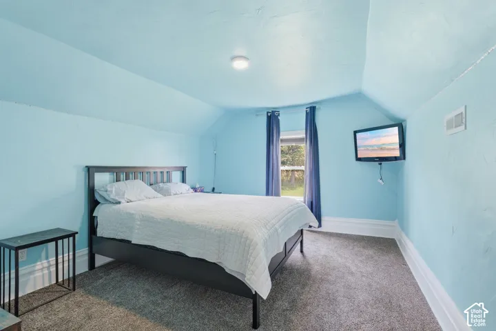 Vaulted ceiling with an integrated light fixture, carpeted flooring, and a wall-mounted display