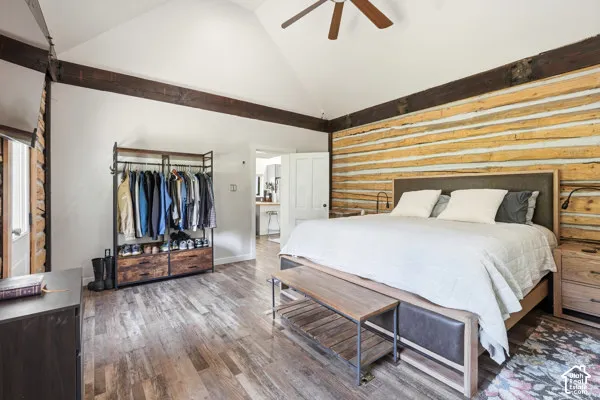 Vaulted ceiling with exposed wood beams, wood-finish flooring, log wall accent, and ceiling fan