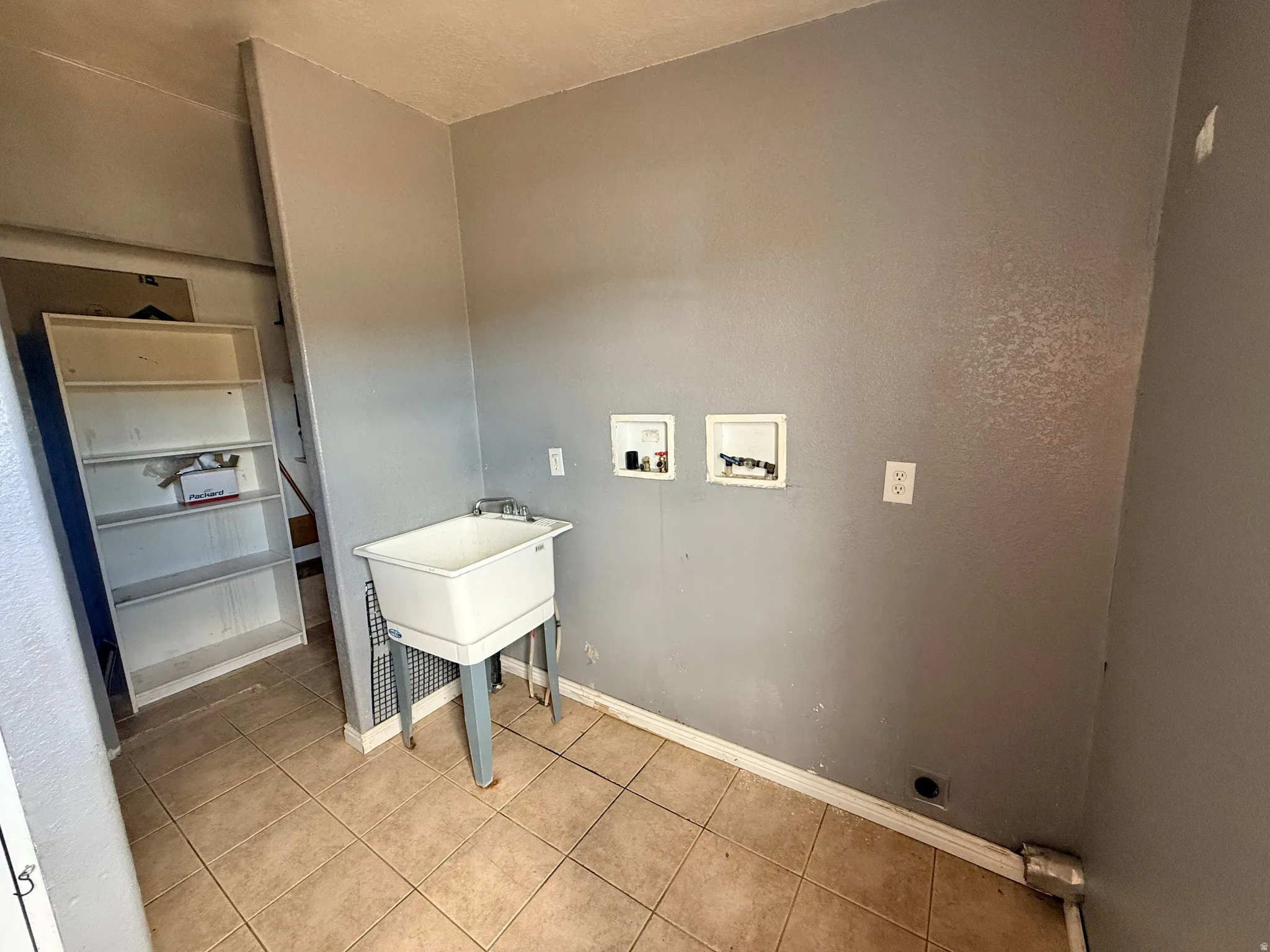 Utility sink with dual-handle faucet, tile flooring, and dedicated appliance hookups