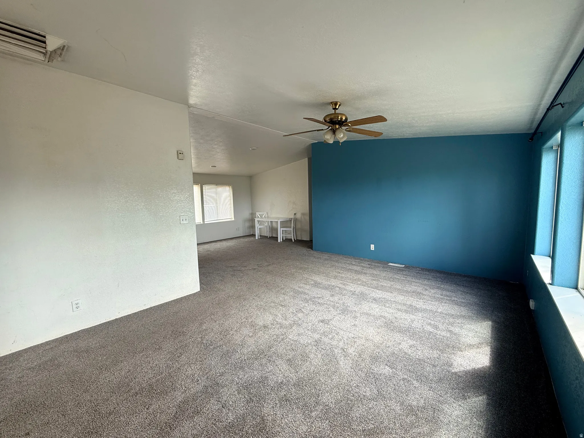 Carpeted interior with a ceiling fan, accent wall, and window with a sill