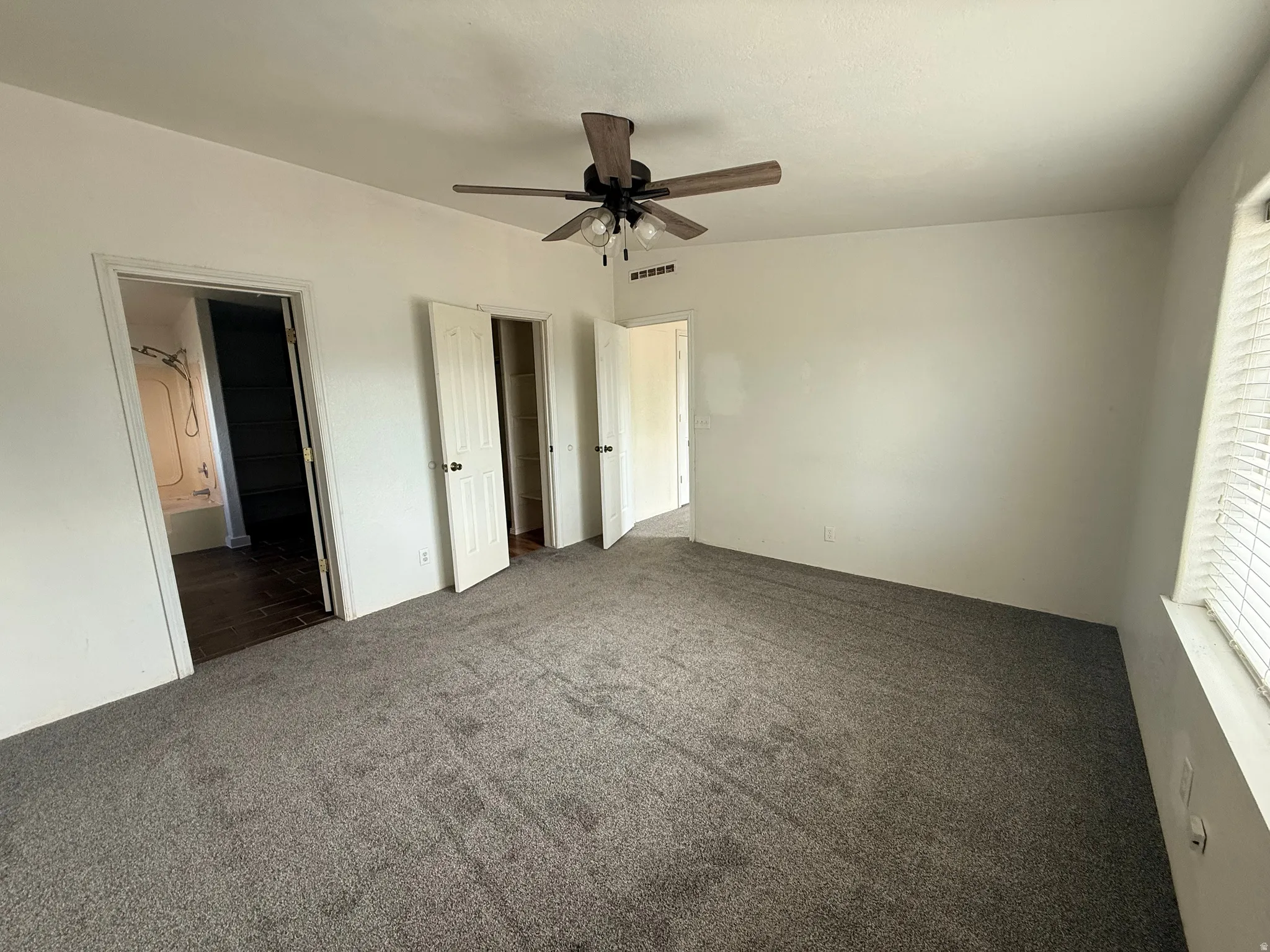 Carpeted room featuring a ceiling fan, multiple doorways, and a window with blinds
