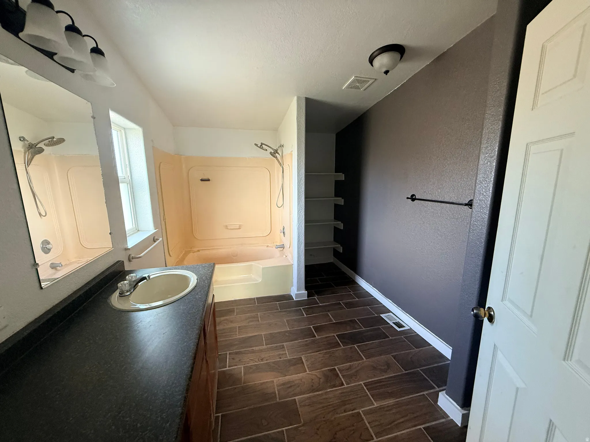Bathroom with a single vanity, undermount sink, dark countertop, and wood-finish tile flooring