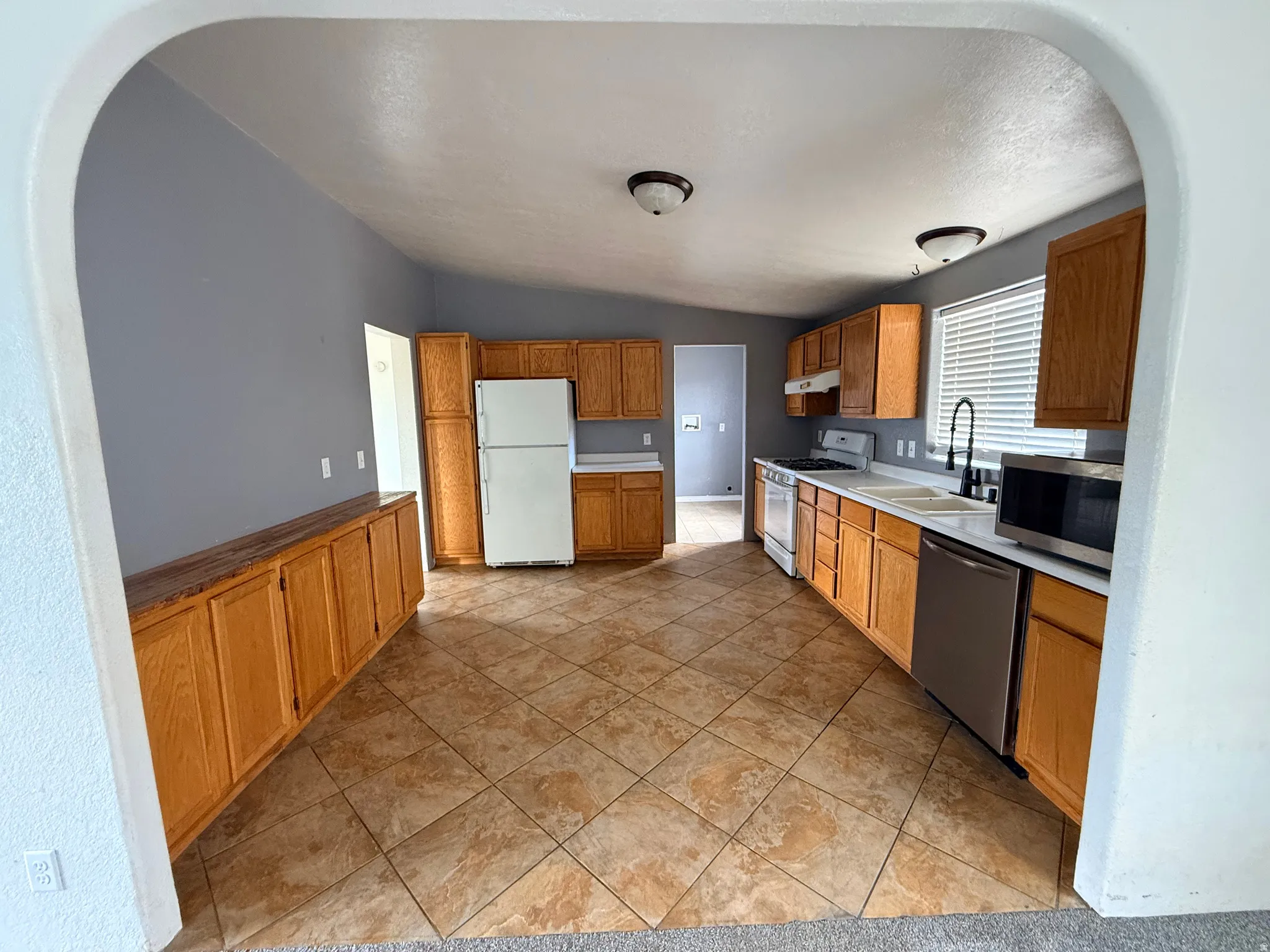 Kitchen featuring wood cabinetry, light-toned countertops, a stainless steel dishwasher, and a built-in microwave