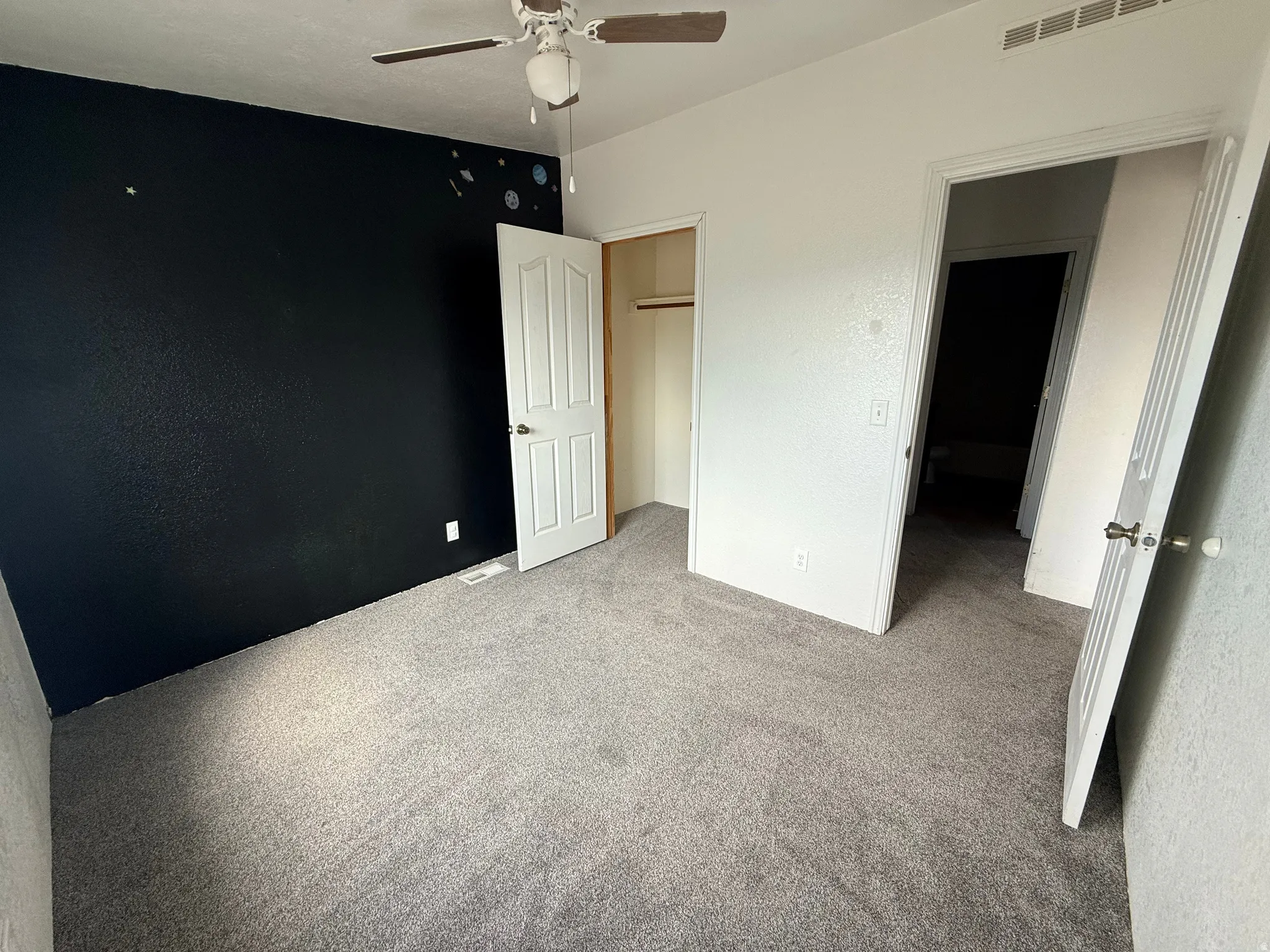 Carpeted room with a ceiling fan, white paneled doors, and an open closet with a hanging rod