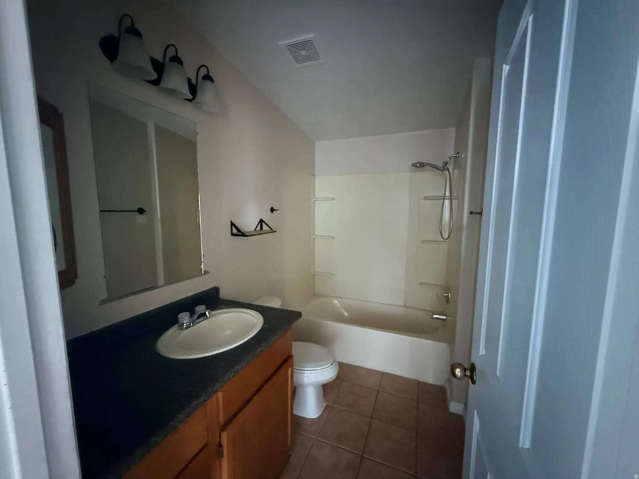 Bathroom featuring a vanity with an integrated sink, a full-width mirror, a three-light vanity fixture, a bathtub with a shower, and tile flooring