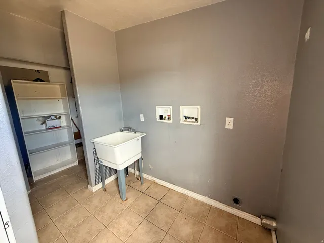 Utility sink with dual-handle faucet, tile flooring, and dedicated appliance hookups