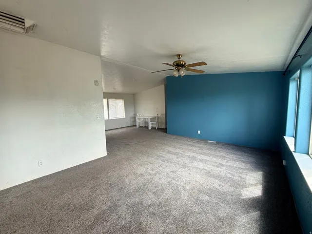 Carpeted interior with a ceiling fan, accent wall, and window with a sill