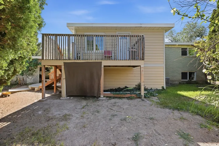 Rear exterior with an elevated wood-finish deck and balustrade, featuring a sliding glass door and an attached wood-finish staircase