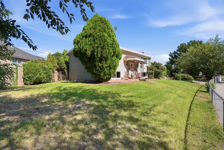 Expansive grassy yard with mature trees and a chain-link fence