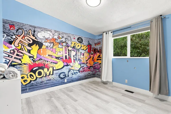 Room featuring a bright accent wall, wood-finish flooring, and natural light