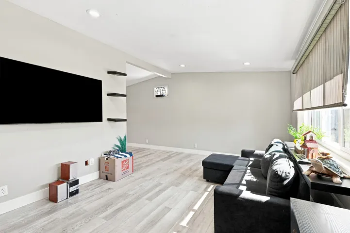 Recessed lighting, wood-finish flooring, a large window with vertical blinds, and built-in shelving