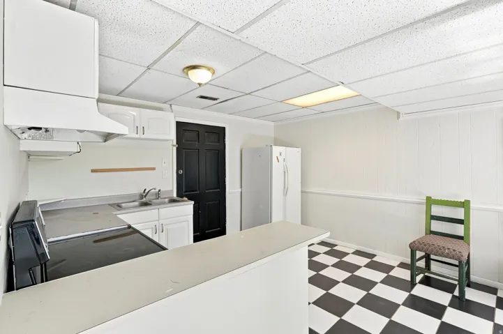 Kitchenette featuring white cabinetry, a built-in range hood, a stainless steel sink, and black and white checkerboard flooring