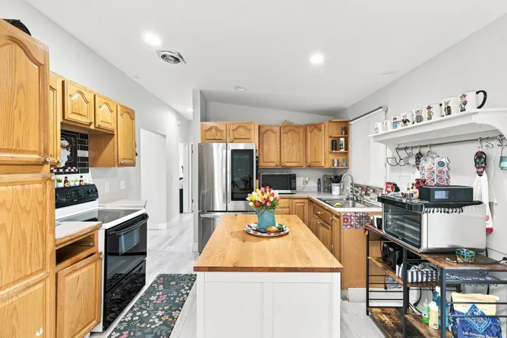 Kitchen featuring ample wood cabinetry, stainless steel appliances, a white island with a wood countertop, and recessed lighting